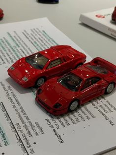 two red toy cars sitting on top of a piece of paper next to each other