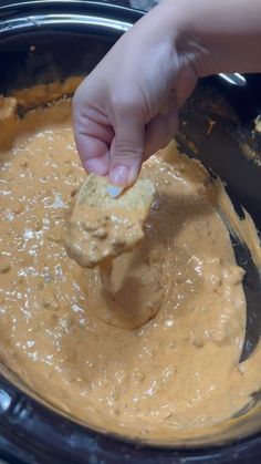 a person dipping something into a bowl with peanut butter in it and holding a tortilla chip