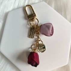 a key chain with two charms attached to it on top of a white plate next to a pink flower