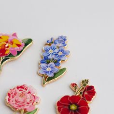 four flower pins sitting next to each other on a white surface with one red, one blue and one yellow