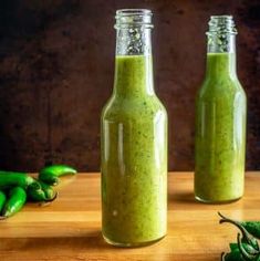 two bottles filled with green sauce next to peppers