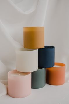 several different colored candles sitting next to each other on a white tableclothed surface