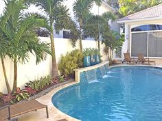 an empty swimming pool surrounded by palm trees and lounge chairs in front of a house