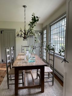 a dining room table with vases and flowers on top of it in front of two windows