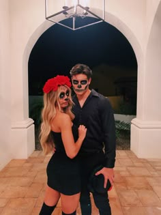 a man and woman in skeleton makeup posing for the camera with red flowers on their head