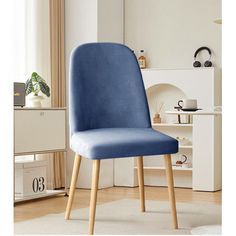 a blue upholstered chair with wooden legs in a white living room, next to a window