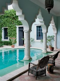 an outdoor swimming pool with chairs and potted plants next to it, surrounded by arches