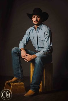 a man sitting on top of a wooden stool wearing a cowboy hat and blue shirt