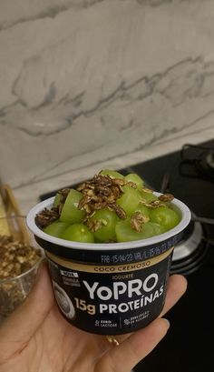 yogurt is being held up in front of a stove top with grapes and granola