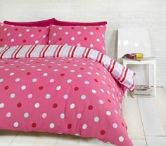 a pink bed with white and red polka dots on the comforter is in front of a brick wall