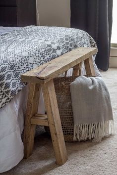 a wooden bench sitting on top of a bed next to a pillow and blanket in a bedroom