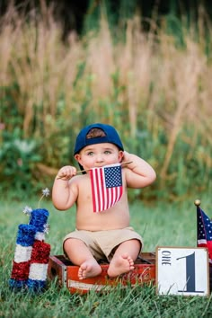 a little boy sitting in the grass with an american flag on his shirt and hat