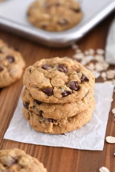 chocolate chip cookies stacked on top of each other in front of a pan of oatmeal flakes