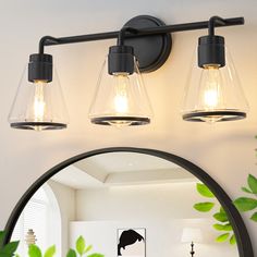 three light bathroom fixture with clear glass shades and black metal frame, on a white wall