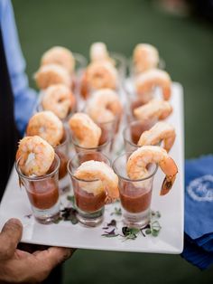 small glasses filled with shrimp and sauce on a white platter, held by a man