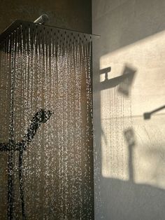 a shower head with water running down it's side and the shadow of a street light on the wall