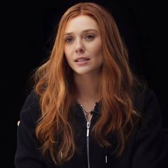 a woman with long red hair is looking at the camera while wearing a black jacket