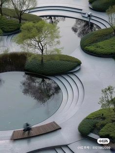 an aerial view of a park with benches and trees in the center, surrounded by water