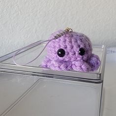 a purple crocheted stuffed animal sitting on top of a plastic container with eyes