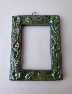 a green frame with flowers and leaves on the inside is hanging from a wall or ceiling