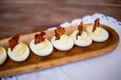 deviled eggs with bacon are arranged on a wooden platter