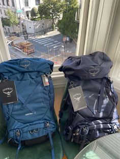 two backpacks sitting next to each other in front of a window on the ground