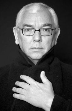 black and white photo of man with glasses holding his hand on his chest