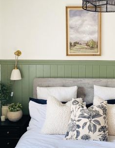 a bed with white sheets and pillows in a bedroom next to a painting on the wall