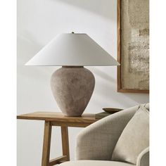 a lamp sitting on top of a wooden table next to a white wall and chair