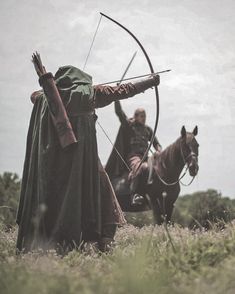 two men dressed in medieval clothing, one holding a bow and the other riding a horse