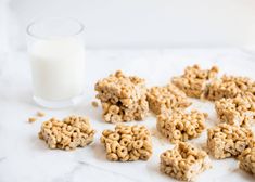 cereal krispy treats next to a glass of milk on a white counter top with some oatmeal in the middle