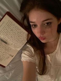 a young woman laying in bed next to an open book with writing on the pages