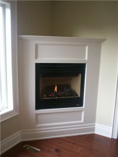 an empty room with a fire place in the corner and hard wood flooring on the other side