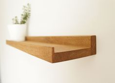 a wooden shelf with a potted plant on it and a white wall in the background