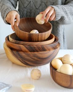 a person is peeling an onion in a wooden bowl on a table with other food items