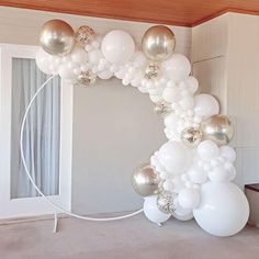 a balloon arch with white and silver balloons hanging from it's sides in an empty room