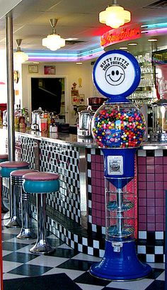 a candy machine in the middle of a checkerboard floored area with stools