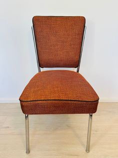 an orange chair sitting on top of a hard wood floor next to a white wall