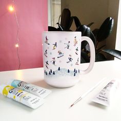 a white coffee mug sitting on top of a table next to some markers and pens