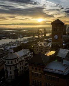 the sun is setting over a city with tall buildings and a clock tower in the foreground