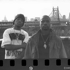 two young men standing next to each other in front of a bridge and cityscape