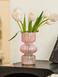 a pink vase filled with white flowers on top of a black table next to a book