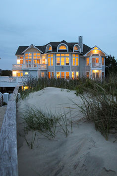 a large house sitting on top of a sandy beach next to a wooden fence and grass