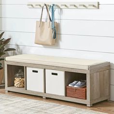 a wooden bench with baskets underneath it and a bag hanging on the wall next to it