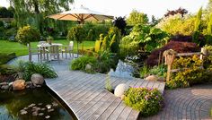 a wooden deck in the middle of a garden next to a pond and table with an umbrella over it