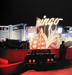 a car is parked in front of the las vegas sign at night with people standing around it