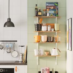 a kitchen with green tiles and shelves filled with dishes, mugs and utensils