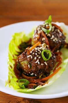 two meatballs in lettuce on a plate with sesame seeds and garnishes