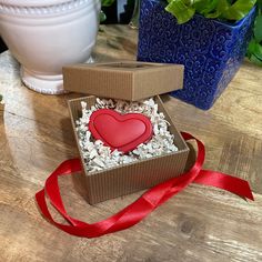 an open box with a heart in it sitting on a table next to a potted plant