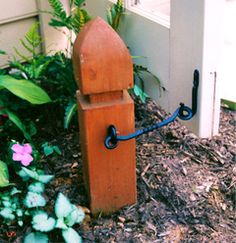 a wooden clock sitting in the middle of a flower bed next to a door way